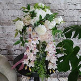 Boho Cascading Wedding Bouquet with Blush Pink and mauve Orchids, blush roses, and white ranunculus with draping greenery.