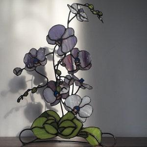 Stain glass orchid,flower made of purple glass with green leaves on a metal stand,flower sculpture, voluminous, consists of several branches