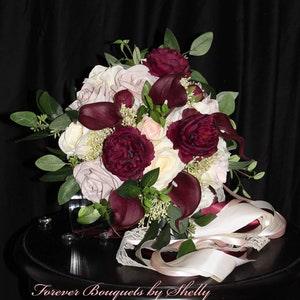 Vintage burgundy wine bouquet with ranunculus, calla lilies. Roses in cream and mauve with ficus and seeded eucalyptus. Long satin ribbon
