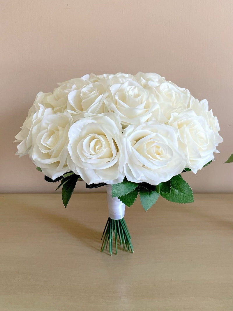 White rose bridal bouquet with green leaves and short ribbon-wrapped stems