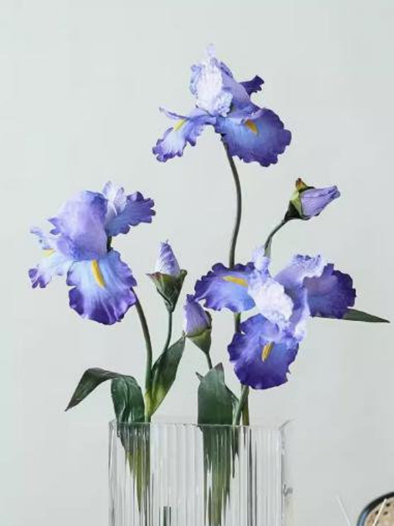 Blue silk iris artificial flowers in clear glass vase, three blooms and green leaves