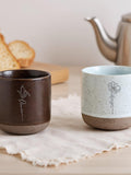 Speckled ceramic mugs with engraved vine-and-flower designs in dark and light tones
