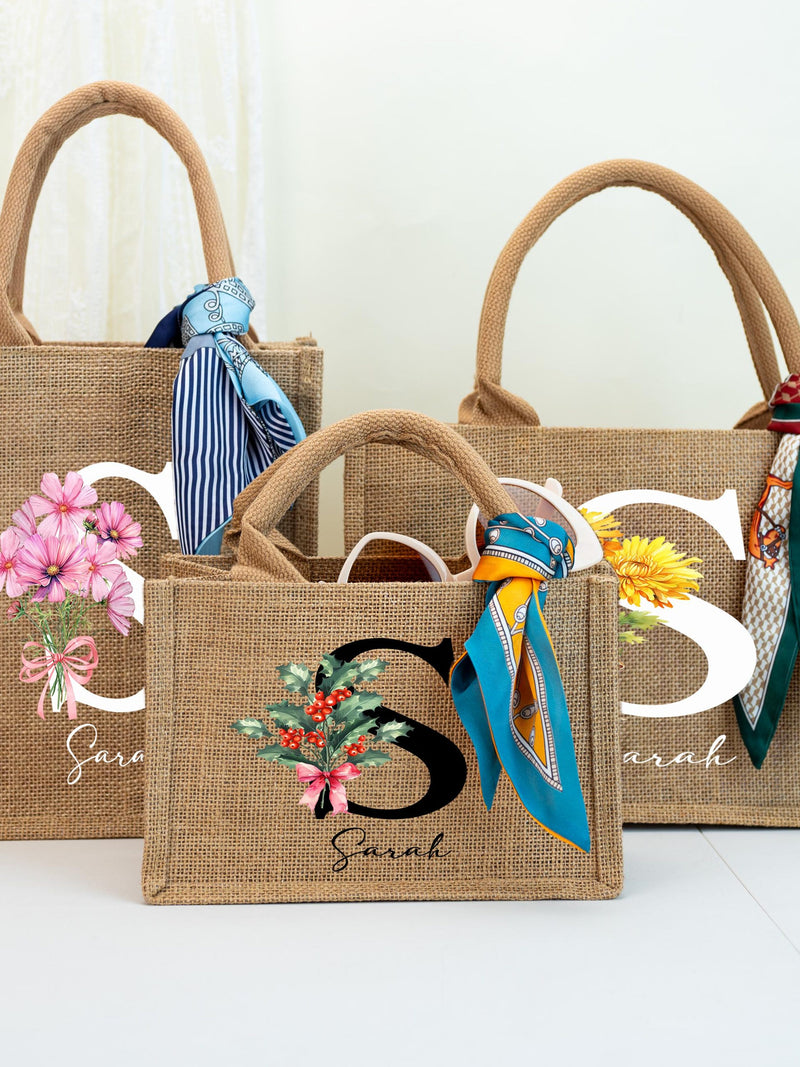 Burlap tote bag with short handles, blue ribbon, floral patch, and script name “Sarah”