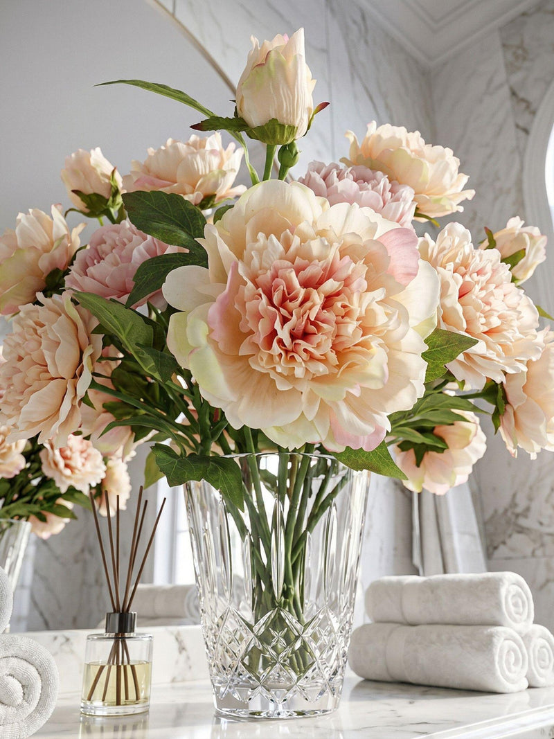 Cream and blush peony bouquet with green leaves in clear glass vase