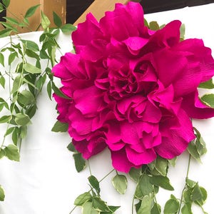 Giant magenta crepe paper peony bloom with layered petals and green leaves