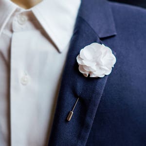 White boutonniere lapel pin with white flower on dark blue suit lapel