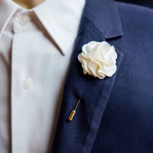 White flower lapel pin on dark blue suit lapel with gold pin back