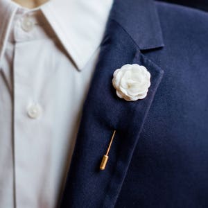 White flower lapel pin on dark blue suit jacket lapel with gold bar pin