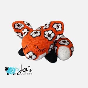 Orange crochet fox amigurumi with white face, black flower-like spots, and closed eyes