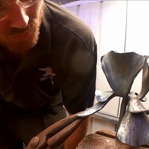 Metal forging die for flower-shaped projects, mounted on anvil with tools nearby