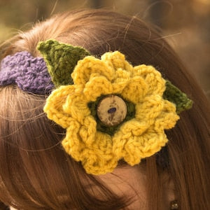 3D crochet flower accessory with yellow petals, green leaves, and round button center