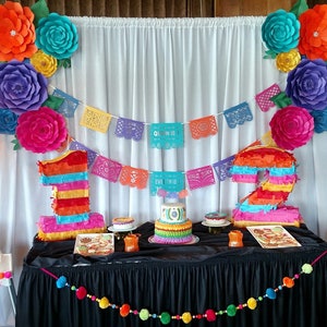 Colorful crepe paper flower backdrop with rainbow number cutouts and festive banner