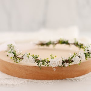 White floral hair wreath with small flowers and greenery on a thin halo headband