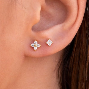 Small flower-shaped CZ stud earrings on model ear, silver-toned metal