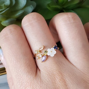 Rose gold floral leaf wrap ring with small flower and leaf charms on finger