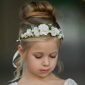 White flower crown headband with green leaves, worn on a girl's hair