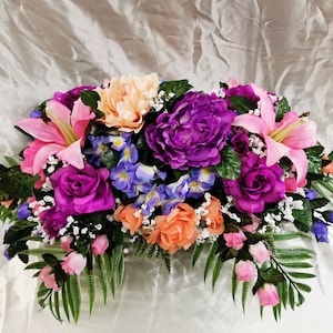 Mixed flower cemetery saddle with purple roses, pink lilies, orange blooms, and greenery