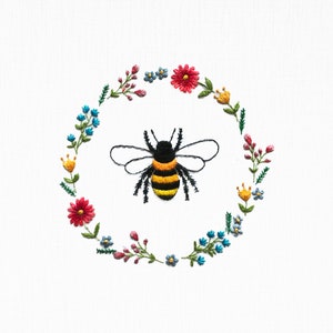 Floral embroidery hoop design with circular wreath of flowers and a black-yellow bee