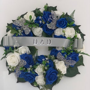 Round artificial funeral wreath with white and blue roses, green leaves, ribbon banner 'DAD'