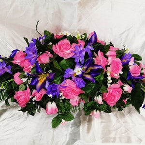 Cemetery saddle floral arrangement with pink roses and purple flowers, green leaves