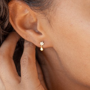 Dainty flower stud earrings with small pearl drop, shown on ear