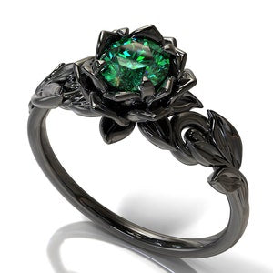 Black lotus-style engagement ring with green oval center stone and braided band