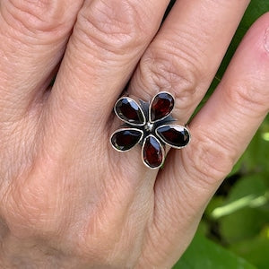 Silver flower ring with red teardrop garnet gemstones on a dark petal setting