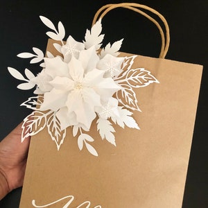 Kraft paper gift bag with white paper poinsettia flower and tan rope handle