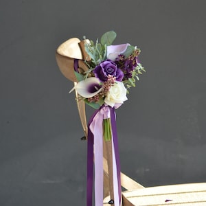 Purple floral chair decoration with calla lilies, roses, greenery, and ribbon streamers
