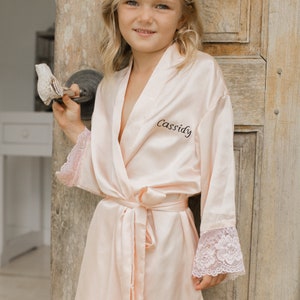 Light pink satin kids robe with V-neck, lace-trim sleeves, and matching tie belt