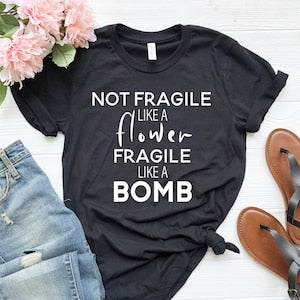 Black graphic T-shirt with white text: “Not fragile like a flower like a bomb”