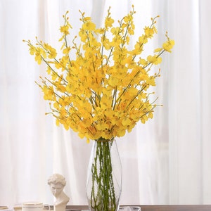Artificial orchid flower arrangement with yellow blooms on tall stems in a clear vase