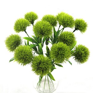 Artificial green allium pompon flowers with green stems in clear glass vase