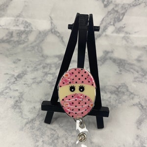 Nurse badge reel with pink cartoon face charm and black lanyard strap