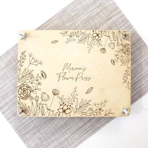 Botanical flower press with beige cover, line-art flowers and leaves, metal corner clips