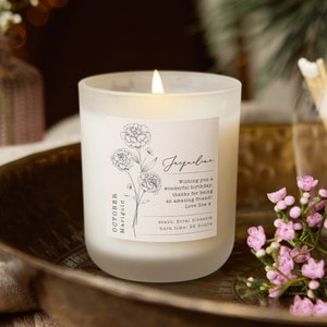 White scented candle in glass jar with engraved birth flower label and flame