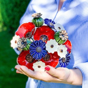 Small faux flower bouquet of red poppies, blue cornflowers, and white blooms in a hand