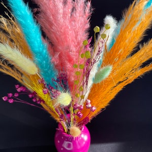 Rainbow dried flower bouquet in a glossy pink vase with bright orange, blue, and pink stems