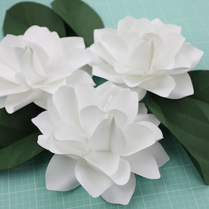 White paper gardenia-style flowers with layered petals and green leaf accents