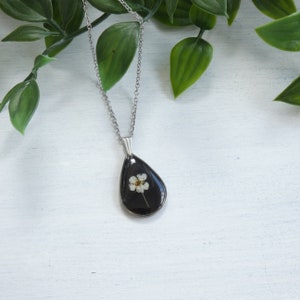 Black resin teardrop pendant with dried white flowers inset on a silver chain