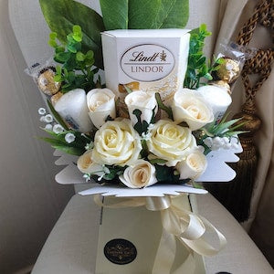White artificial rose bouquet gift hamper with decorative leaves and ribbon
