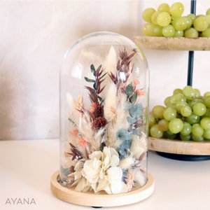 Decorative glass cloche dome with dried bouquet under clear bell on wooden base