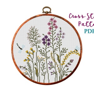 Counted cross-stitch pattern in an embroidery hoop, featuring purple and green wildflowers