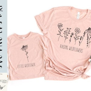 Light pink crewneck T-shirt with black wildflower line art and 'Raising Wildflowers'