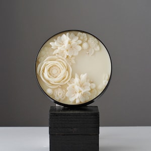 Cream flower soy candle in a round glass jar with white embossed blossoms on top