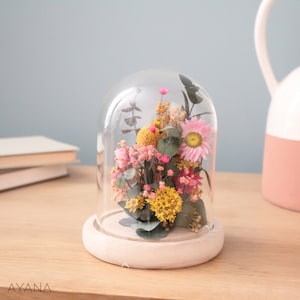 Glass bell with dried flower arrangement in yellow and pink, on white base
