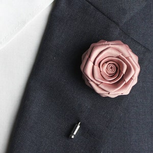 Rose gold rose lapel pin on dark suit fabric, with small clasp pin backing