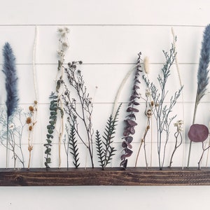 Wooden flower bar with dried wildflower stems arranged along a dark wood plank