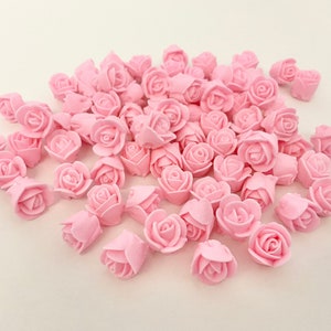Pastel pink mini rose icing decorations, assorted rosette shapes on a flat surface