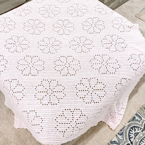 White filet crochet blanket with repeating flower and vine motifs, square edge